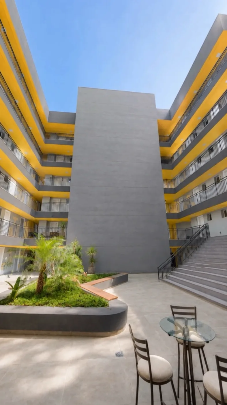 Pátio central do Campus Studios II, com jardim, mesas e a fachada amarela em volta.