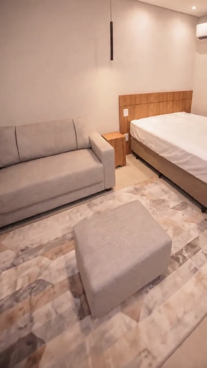Studio mobiliado por dentro: sofá, cama de casal com cabeceira de madeira e piso claro.