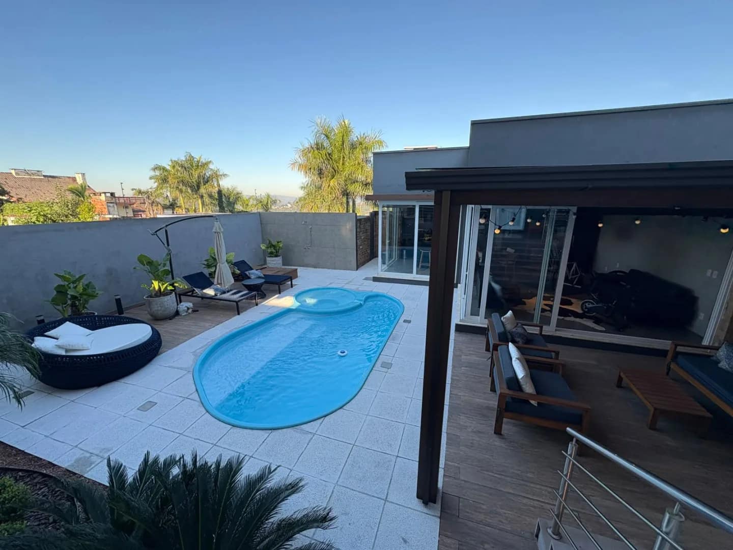 A casa contemporânea vista do pátio, com a piscina em primeiro plano e palmeiras ao fundo.