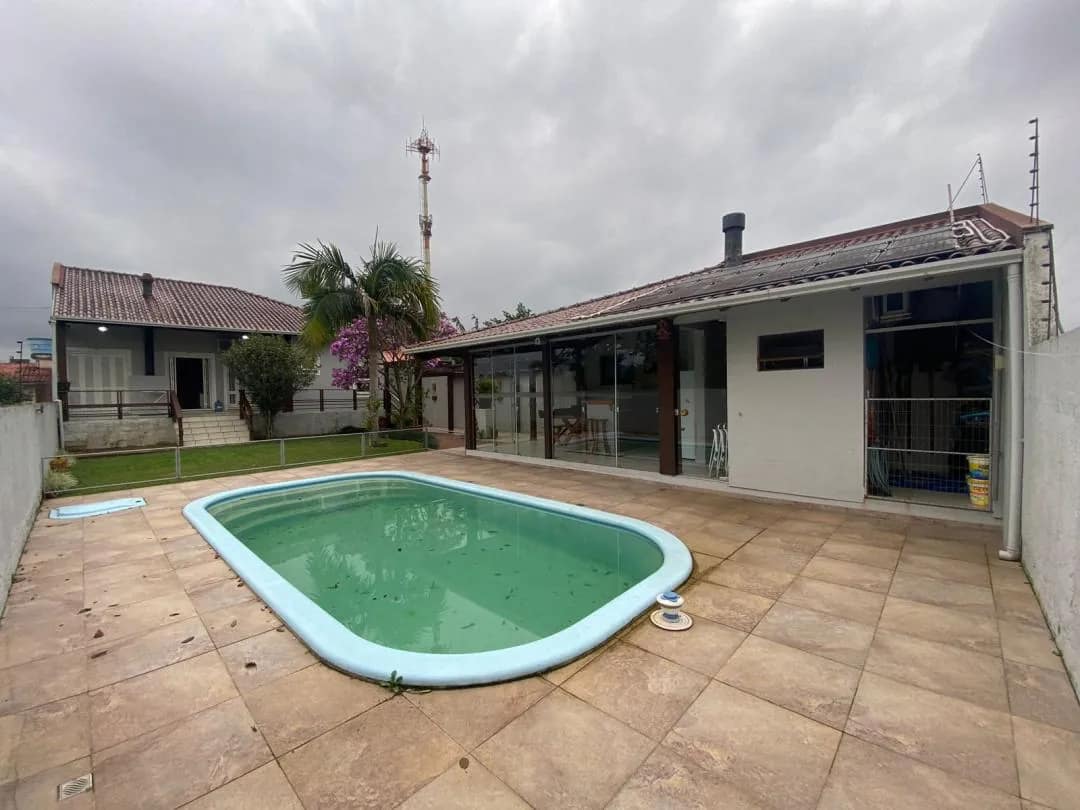 Piscina no pátio de lajota, com a casa térrea e a varanda coberta ao fundo.