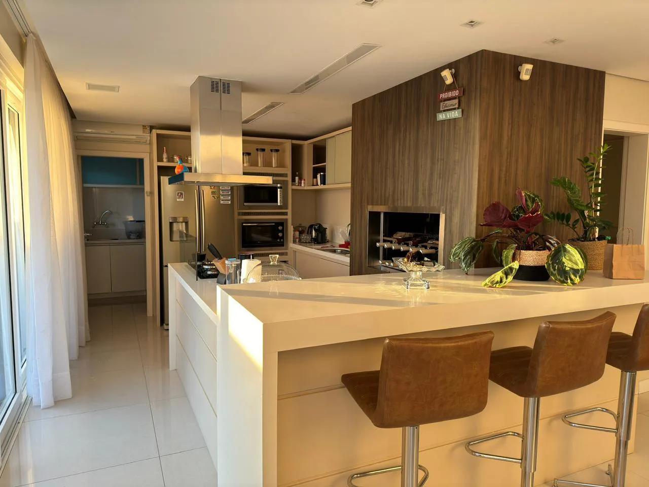Cozinha com ilha central, coifa e banquetas de couro.