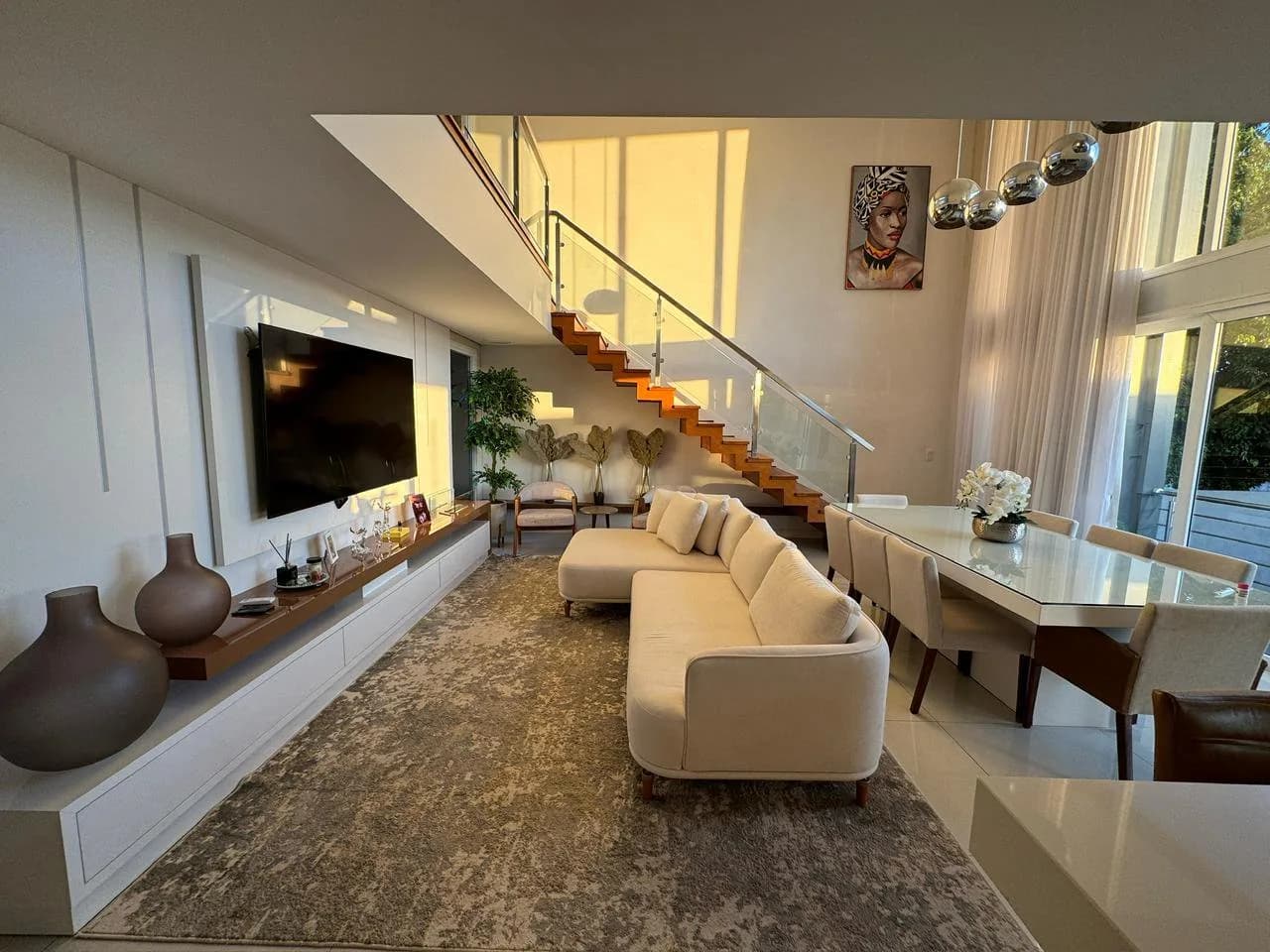 Sala de estar com sofá claro, televisão e a escada ao fundo.