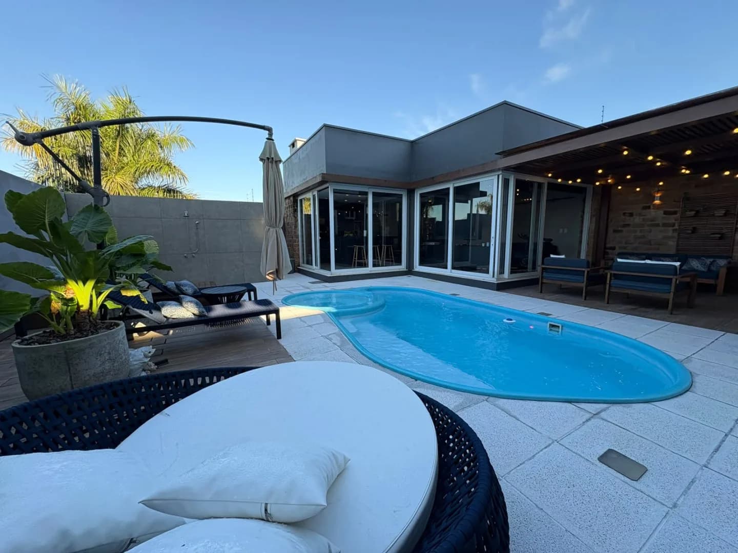 A piscina ao entardecer, com luzes acesas e espreguiçadeiras no deck.