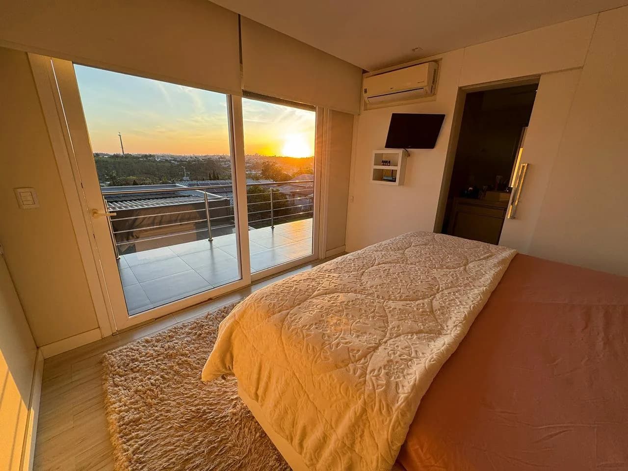Suíte com cama de casal e porta de vidro para a sacada, no fim da tarde.