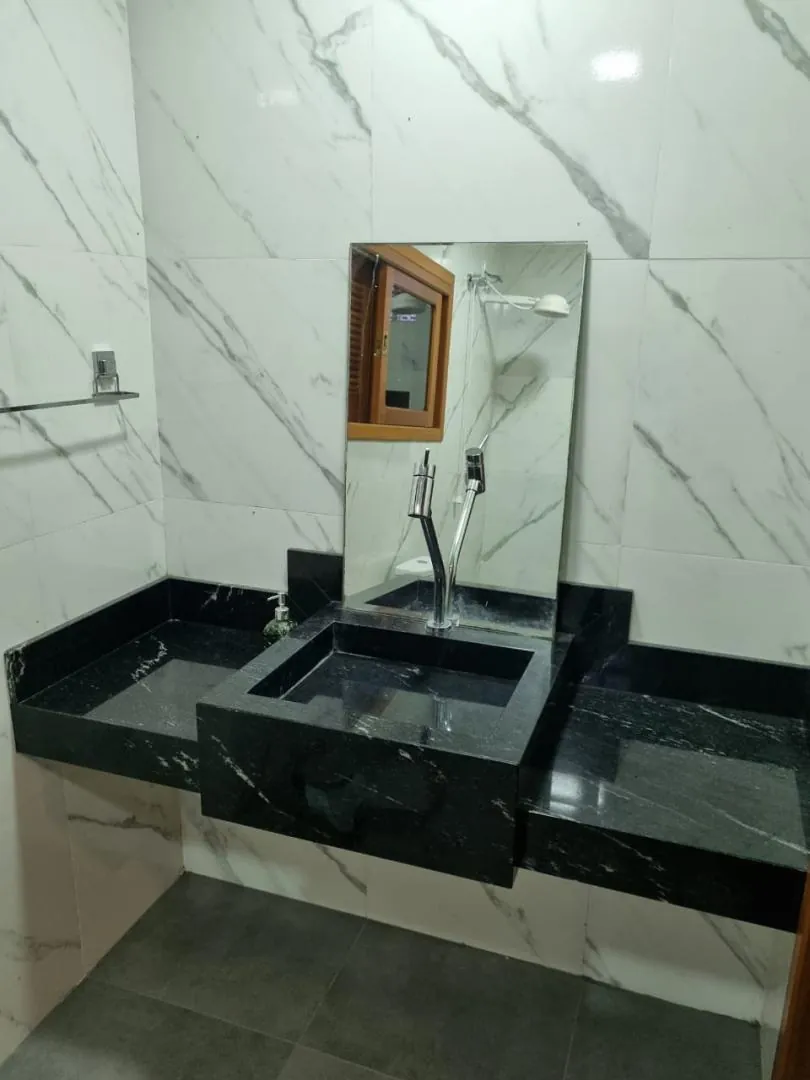 Lavabo com cuba esculpida em granito preto e revestimento marmorizado.