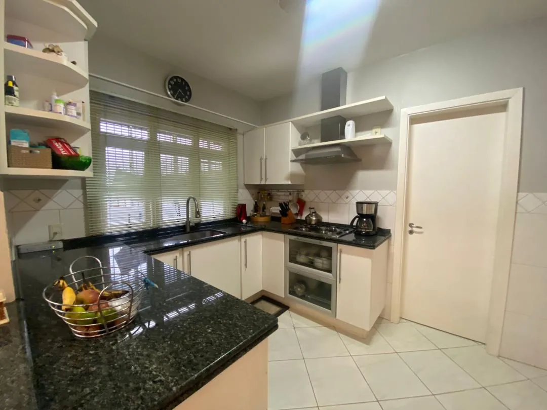 Cozinha com bancada de granito preto, armários brancos e ilha central.