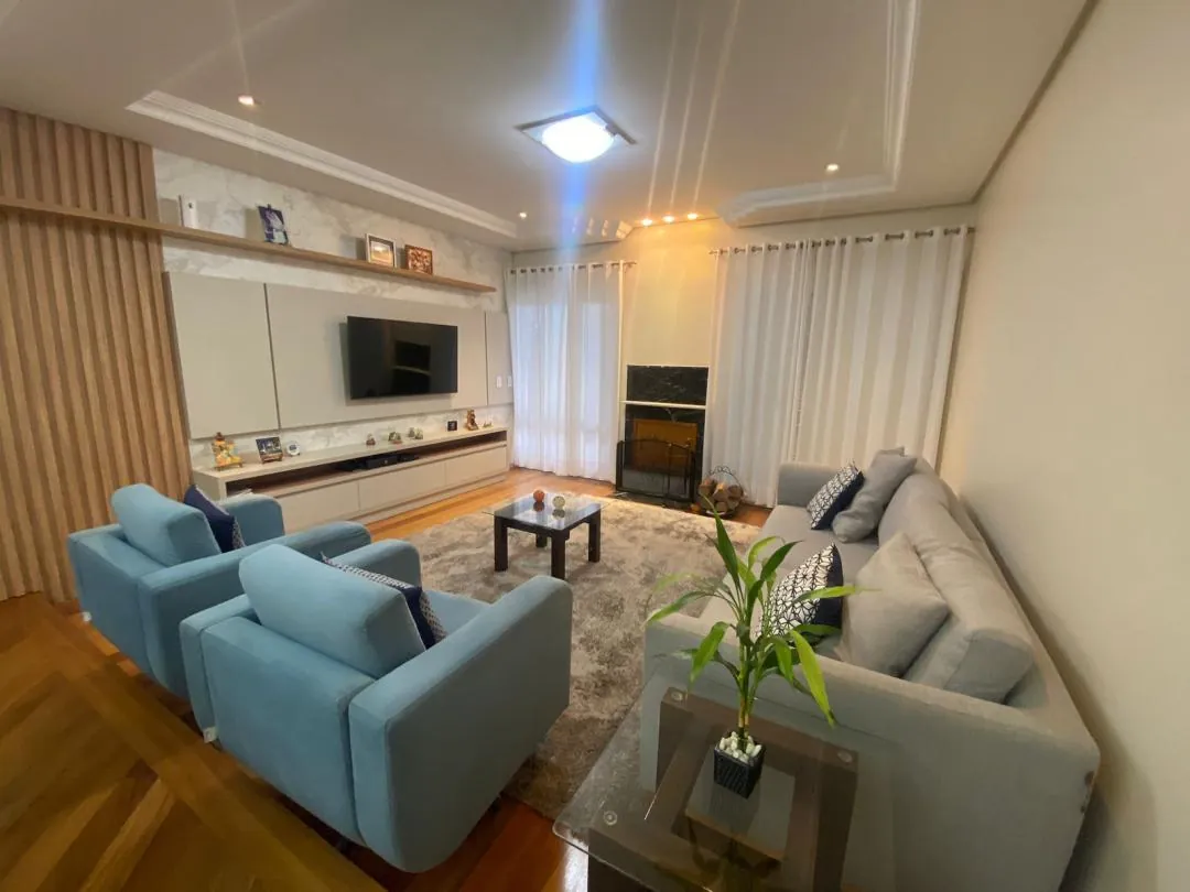 Estar com sofás claros, mesa de centro e televisão na parede.