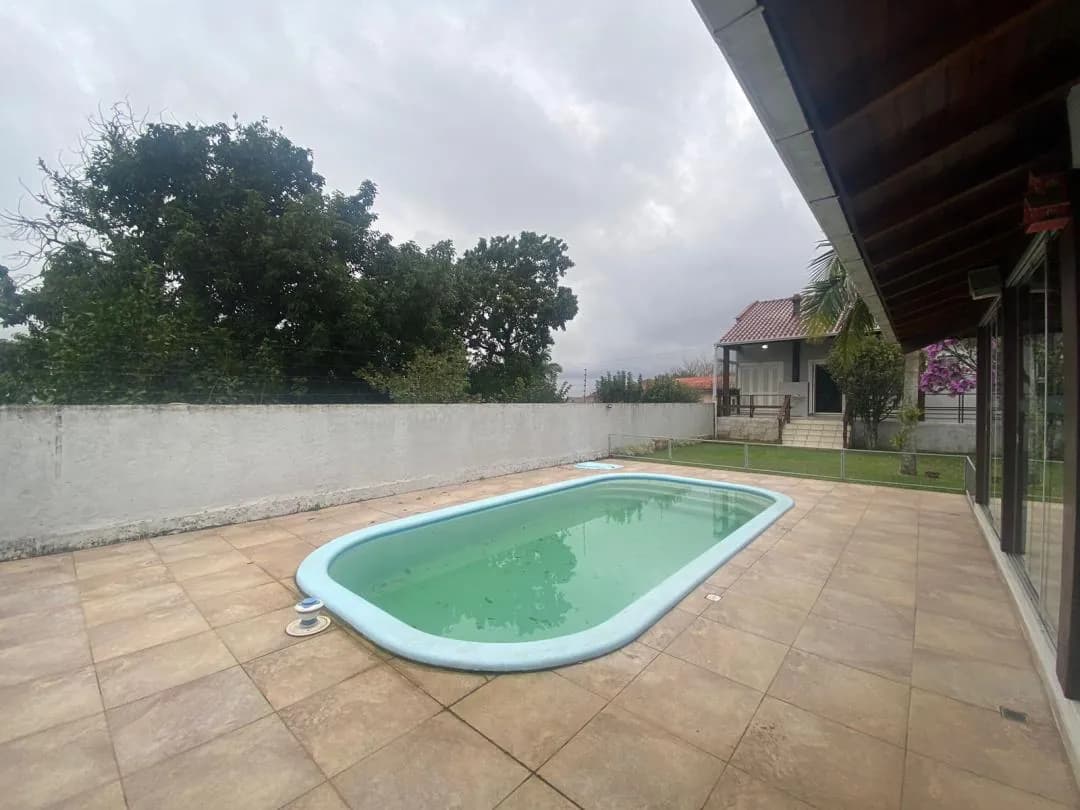 A piscina vista do outro lado do pátio, com árvore e muro ao fundo.