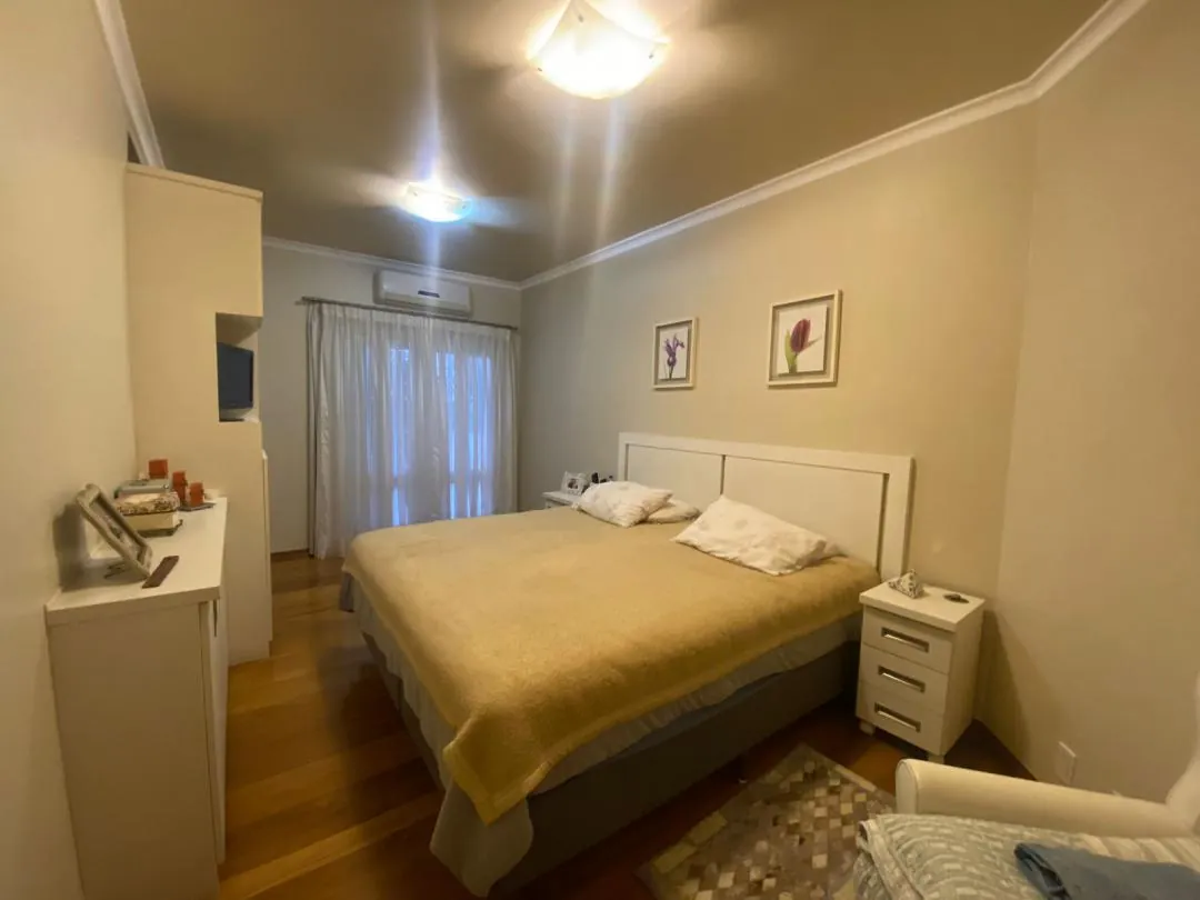 Dormitório com cama de casal, criados-mudos e janela ampla.