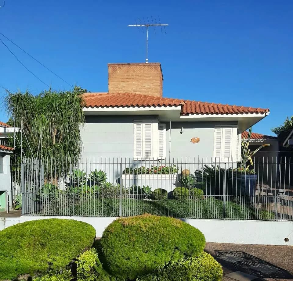 Fachada branca com telhado de barro, grades e o jardim aparado na frente.