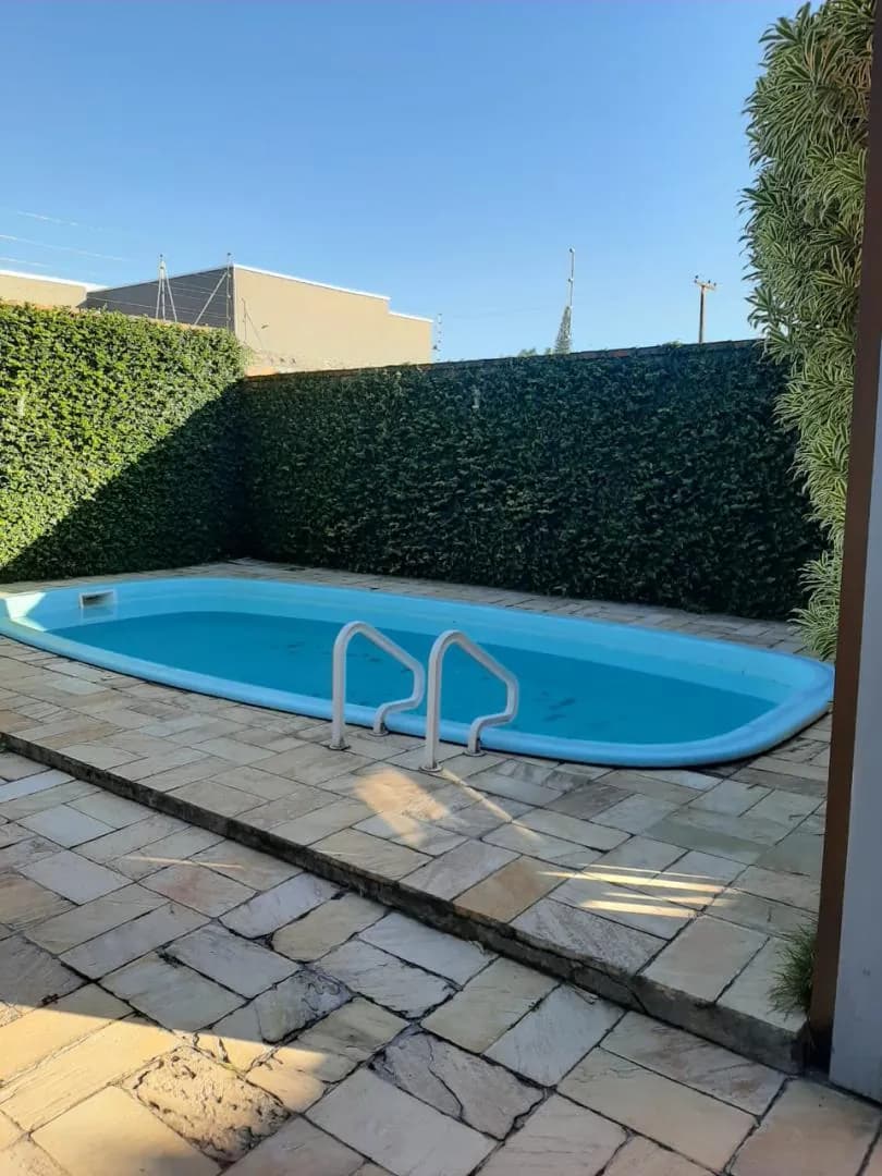 Piscina no pátio lateral, cercada por cerca-viva alta.
