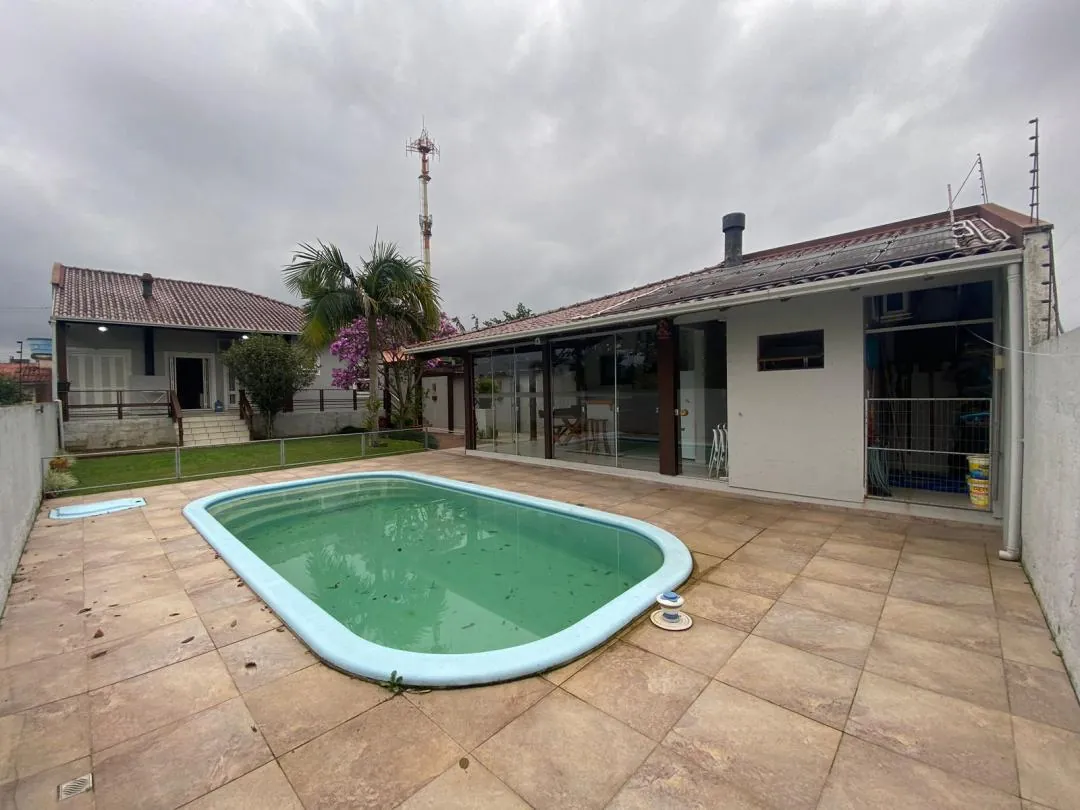 Piscina no pátio de lajota, com a casa térrea e a varanda coberta ao fundo.