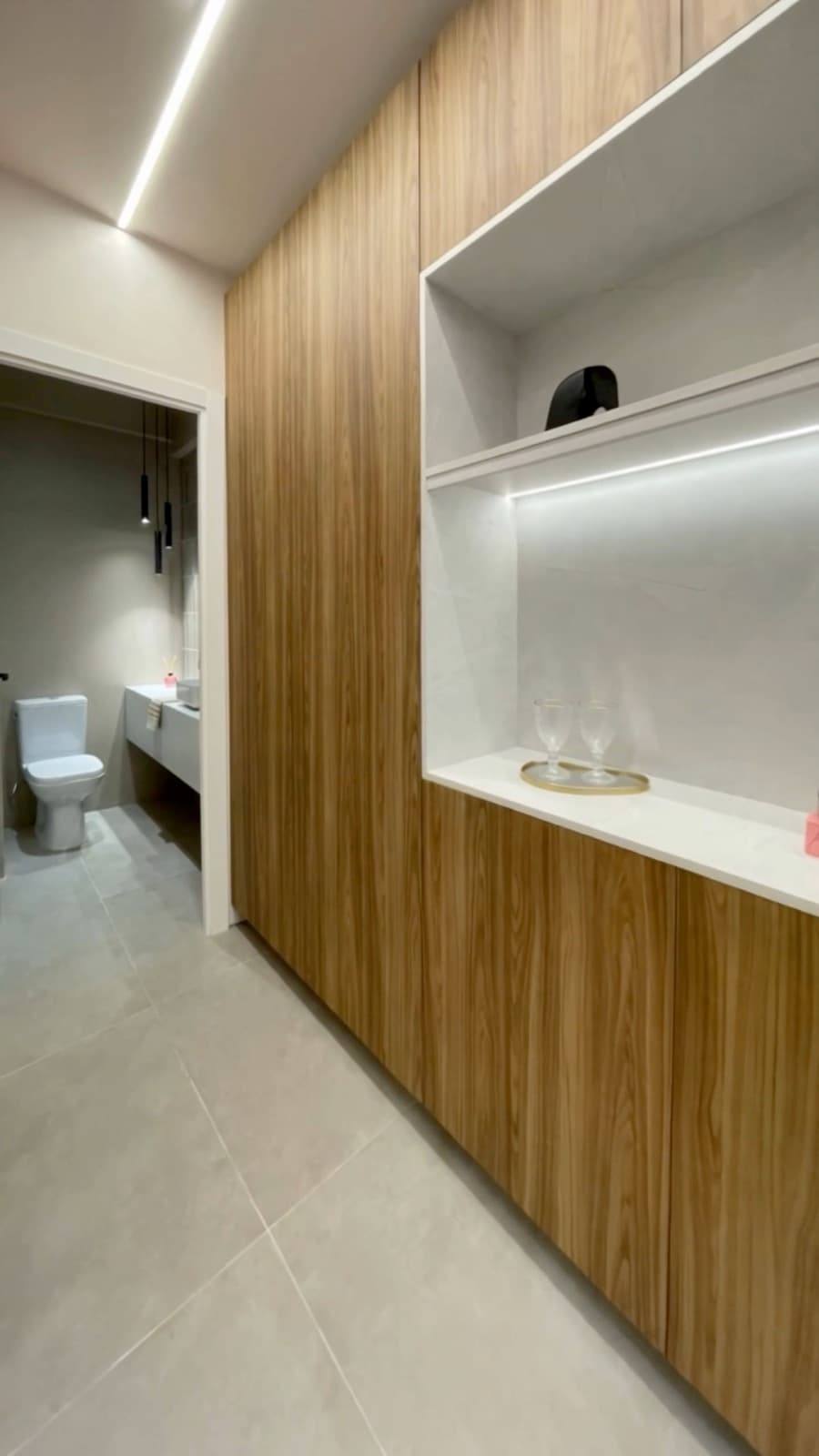 Detalhe do acabamento em madeira, nicho iluminado e lavabo da unidade