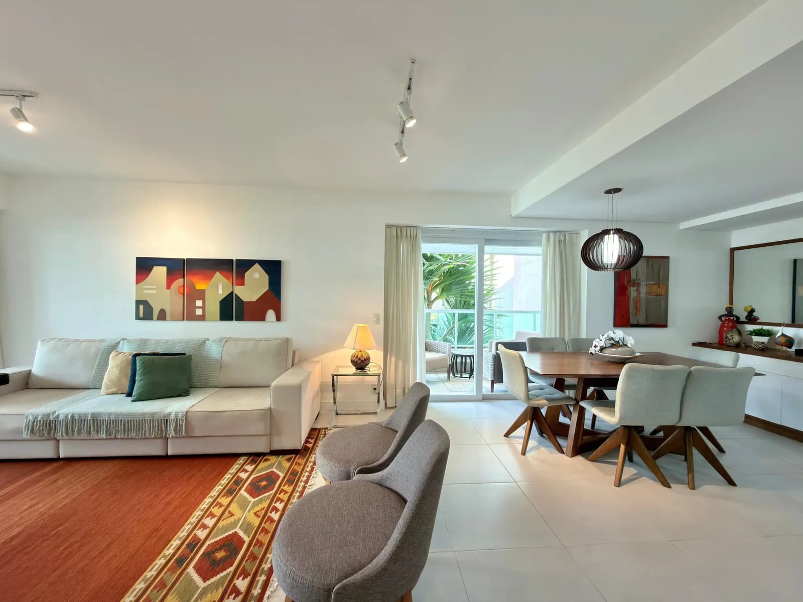 Sala de estar com sofá, tapete kilim e mesa de jantar ao fundo.