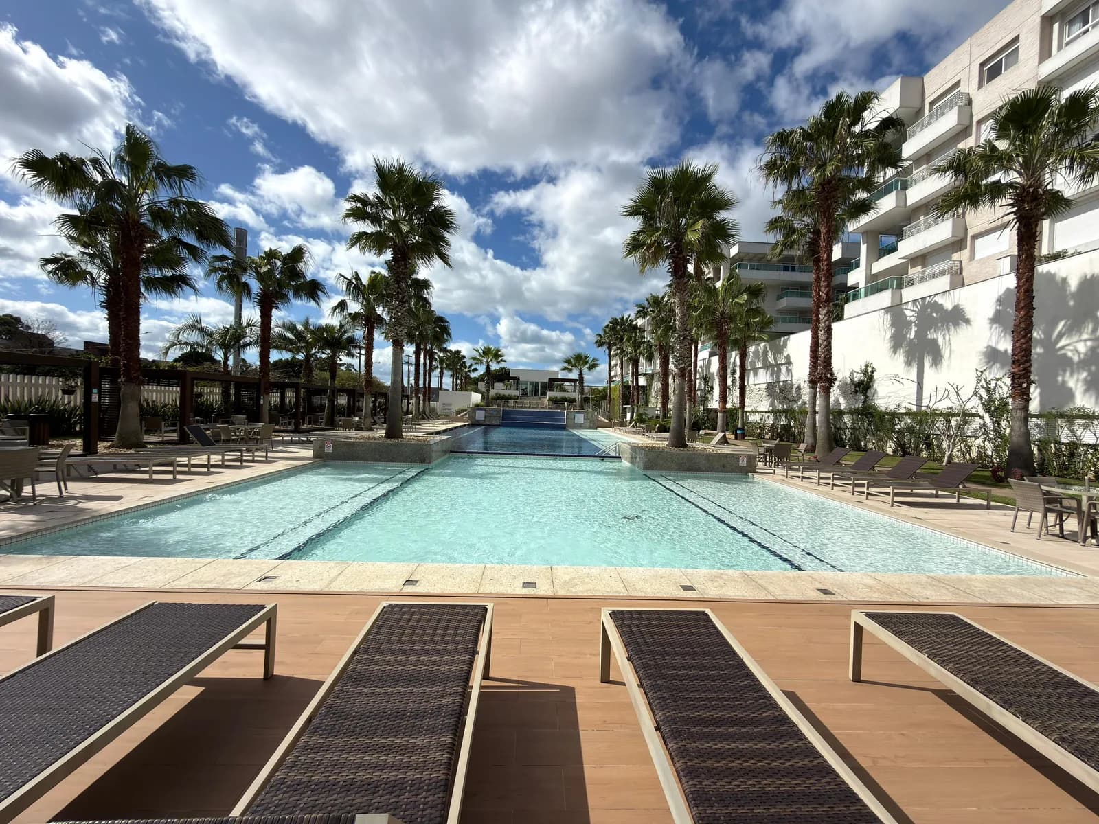Piscina externa do Atlântida Green Square, ladeada por palmeiras e deck de madeira com espreguiçadeiras.