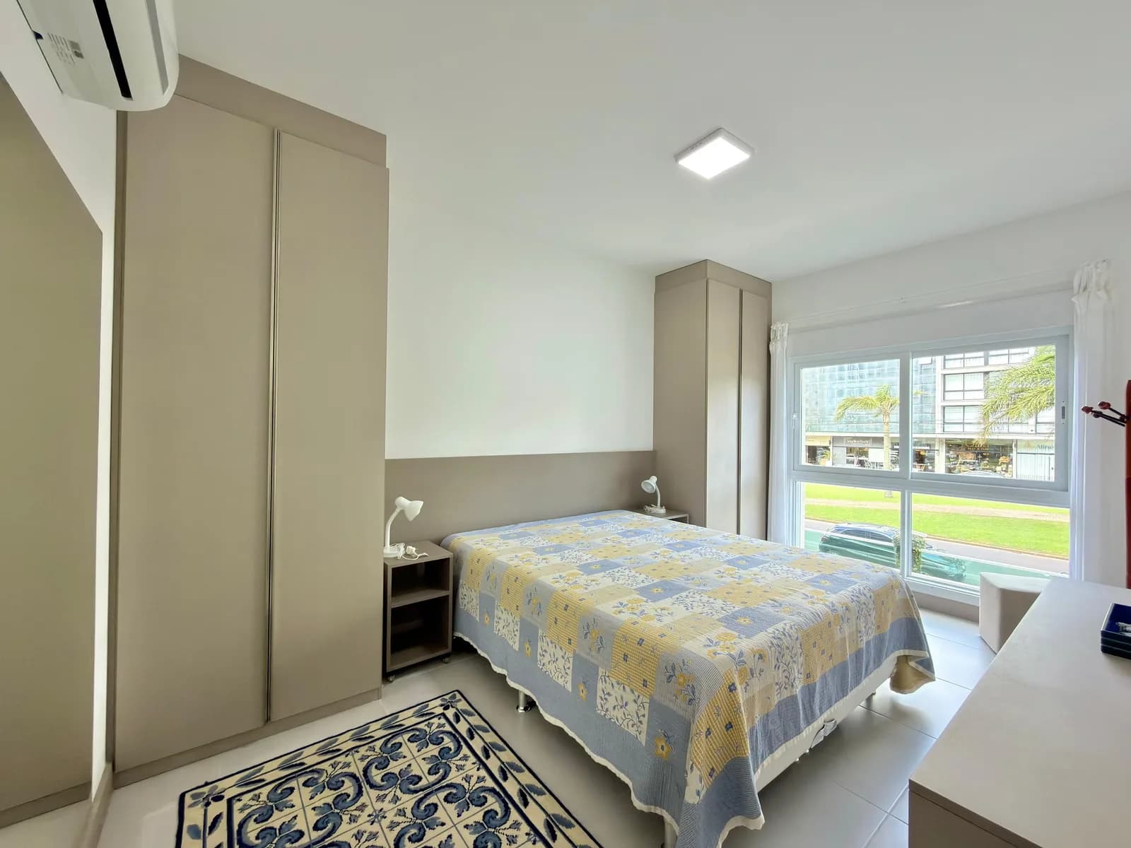 Suíte do apartamento, com cama de casal, closet e janela para a Avenida Central.