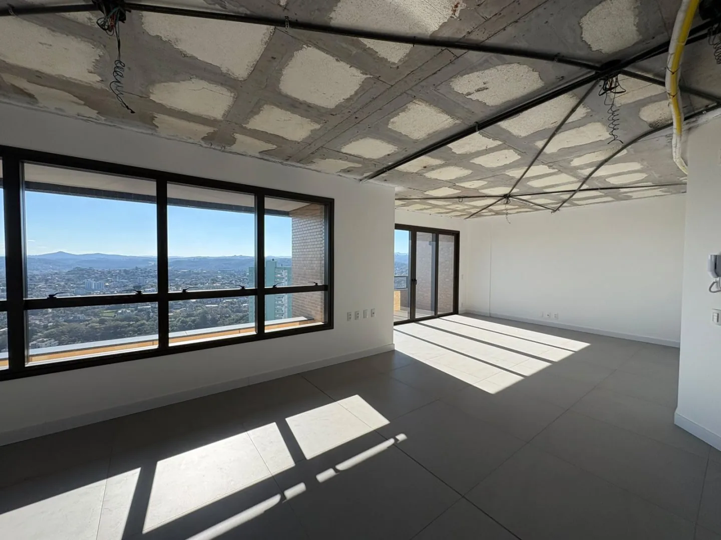Sala em obra com janela de canto, piso assentado e tubulação aparente no teto.