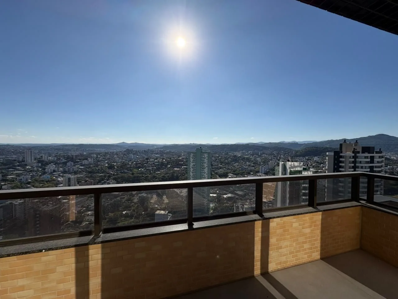 Sacada em L com guarda-corpo de vidro e vista da cidade.