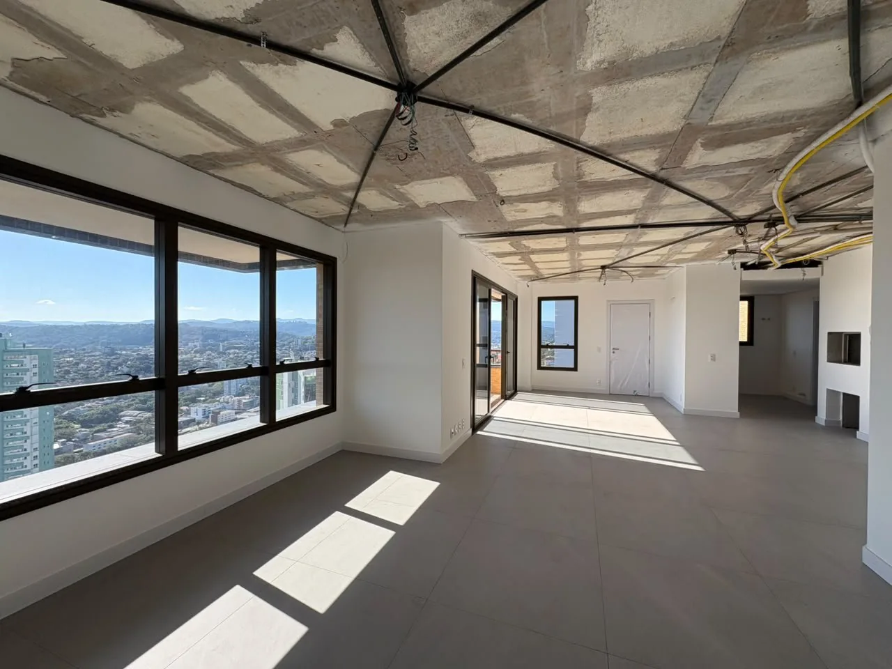 Sala em fase de acabamento, com teto sem forro e janelas amplas.