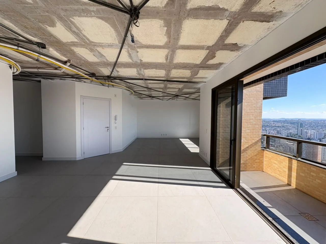 Sala em obra com porta de correr para a sacada e tubulação aparente.