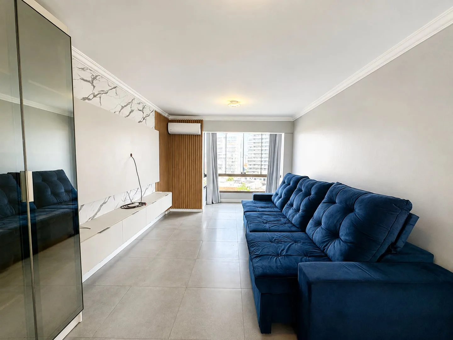 Sala com sofá azul, painel ripado de madeira e rack branco suspenso.