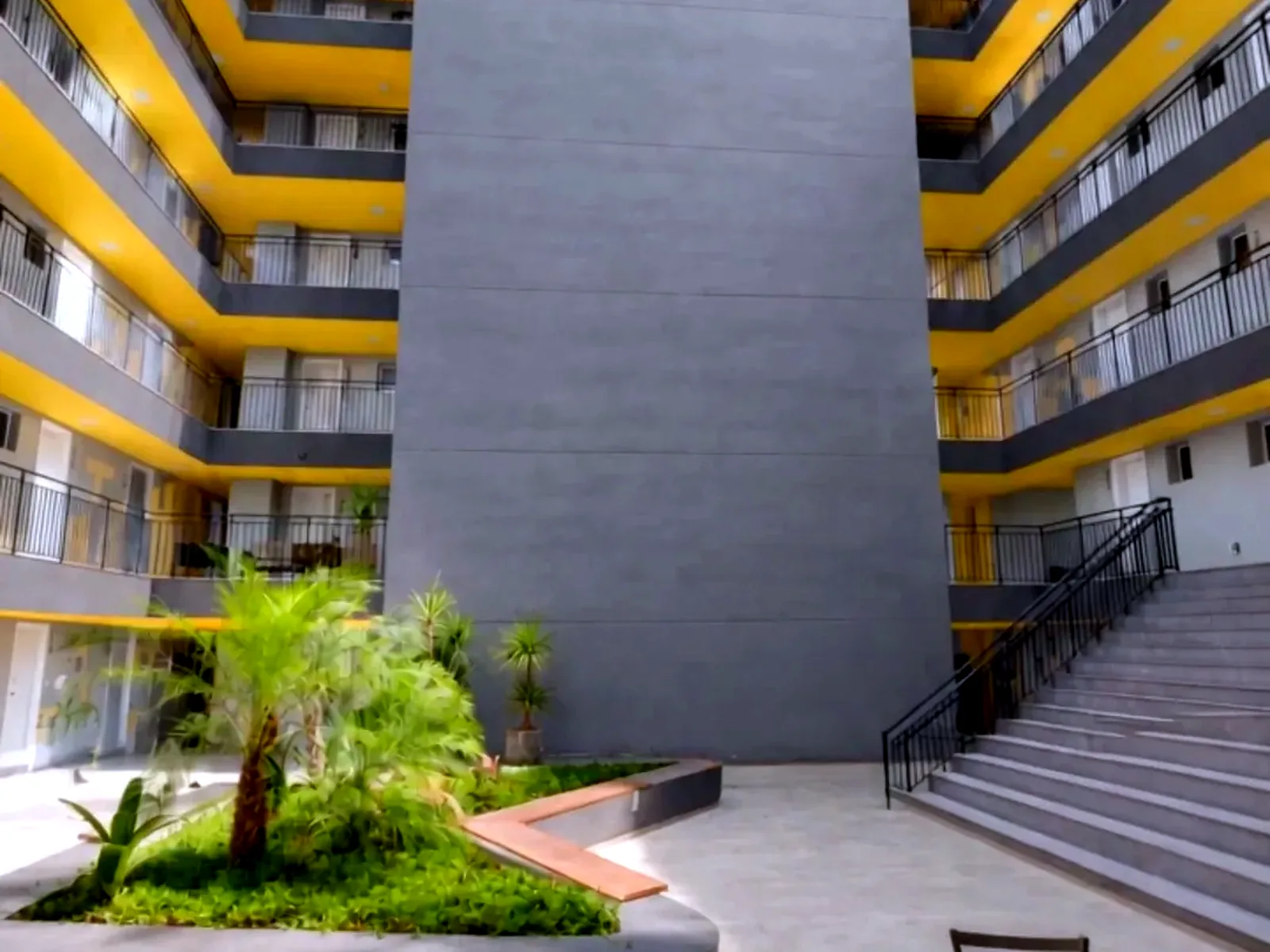 Pátio interno do Campus Studios II, com jardim, escada de acesso e as varandas amarelas dos studios.