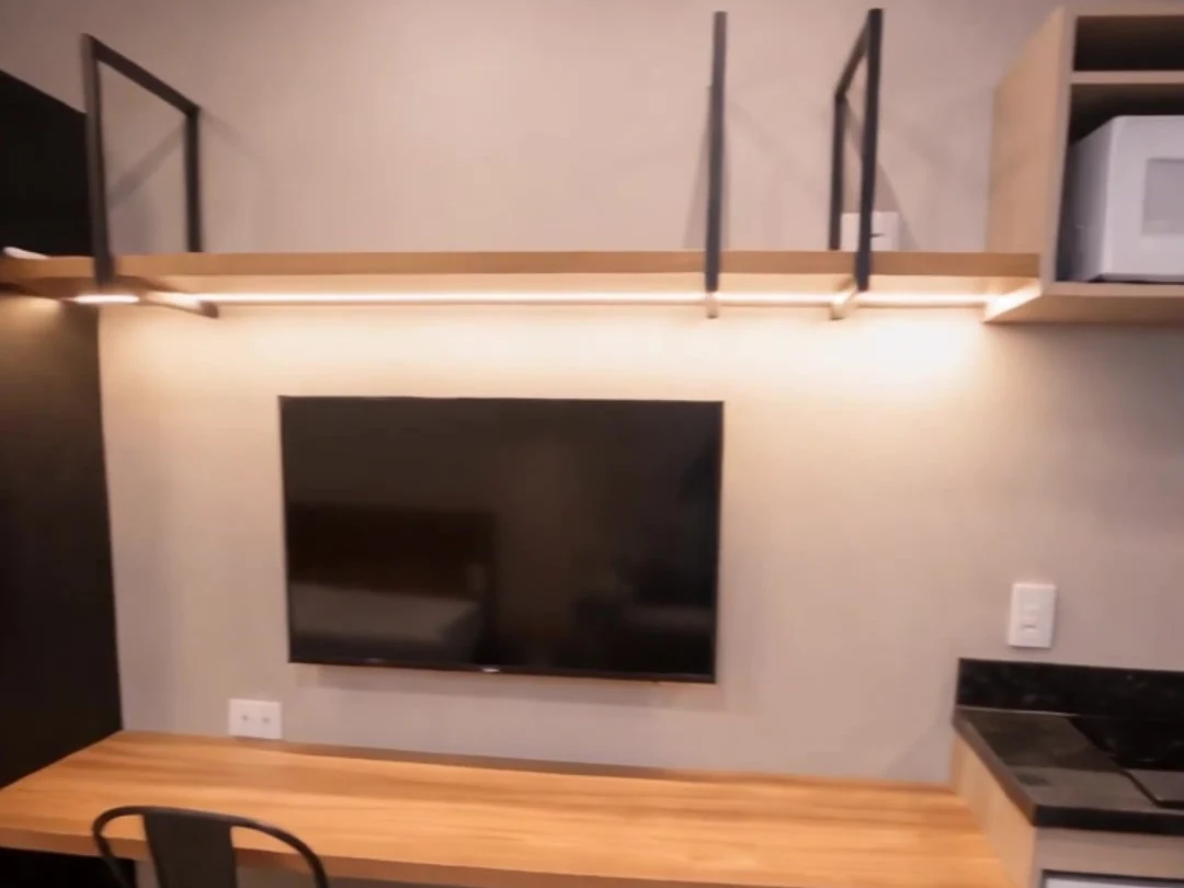 Bancada de trabalho, TV e cozinha do studio mobiliado do Campus Studios II.
