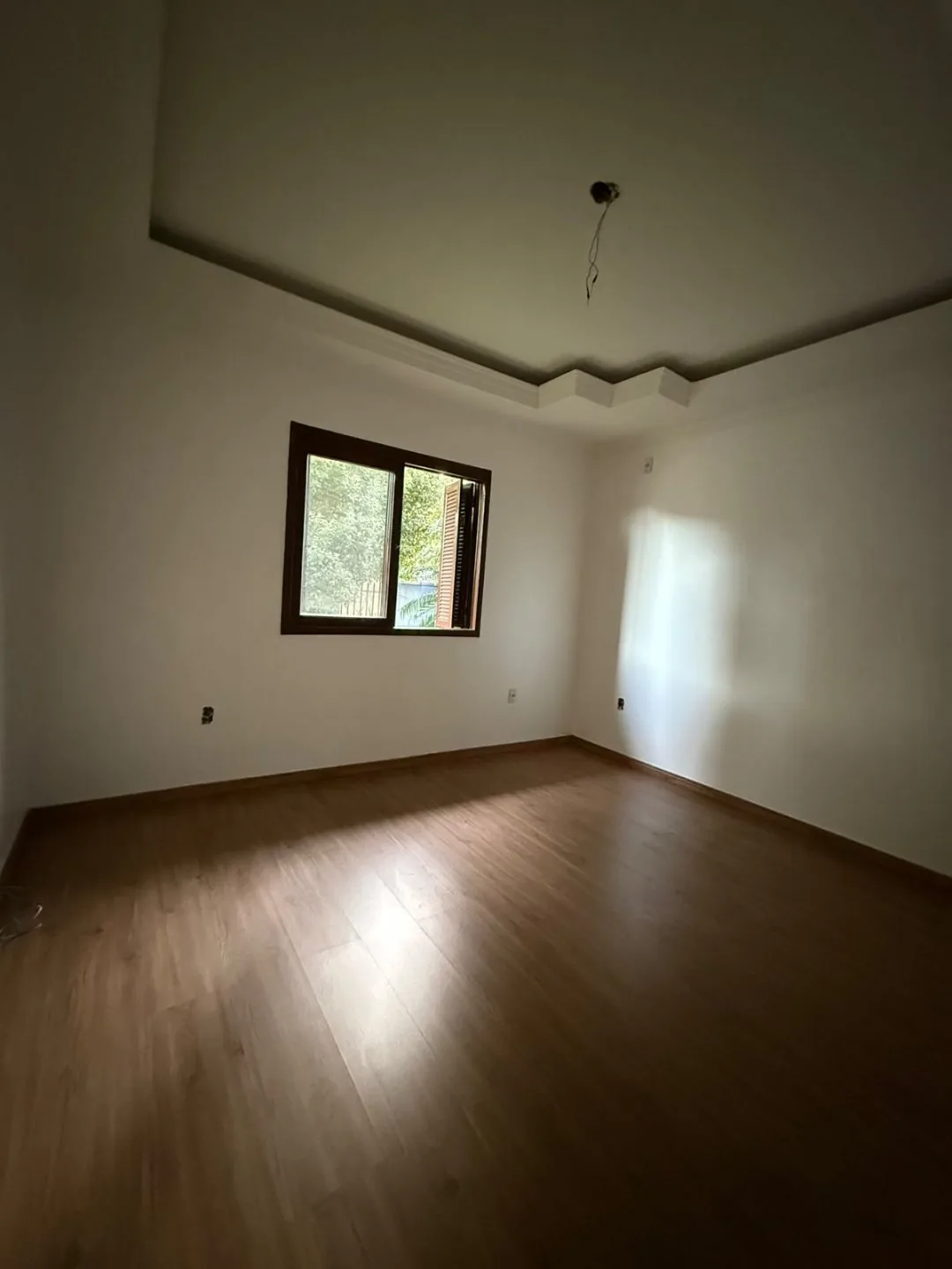 Dormitório vazio com piso laminado, sanca de gesso e janela.
