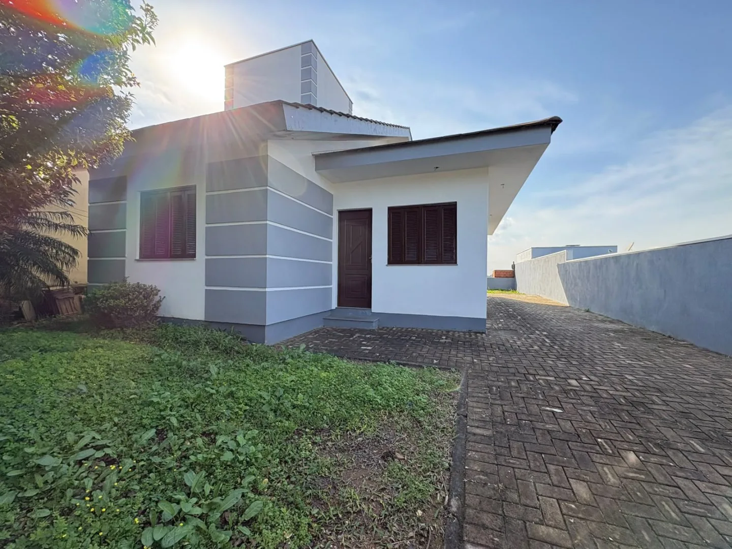 Frente da casa com porta de entrada, janela e acesso calçado ao lado.