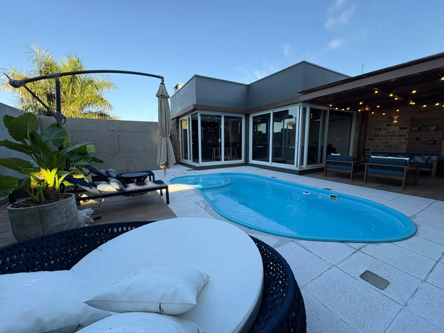 A piscina ao entardecer, com luzes acesas e espreguiçadeiras no deck.