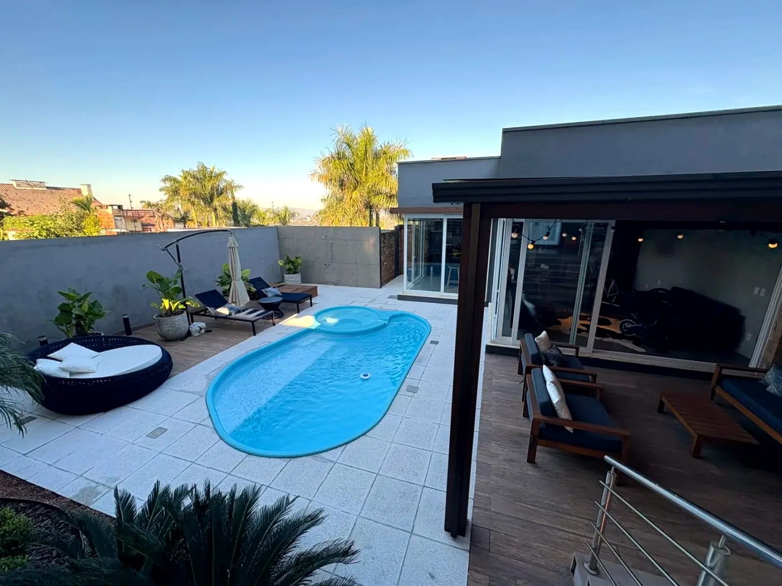 A casa contemporânea vista do pátio, com a piscina em primeiro plano e palmeiras ao fundo.