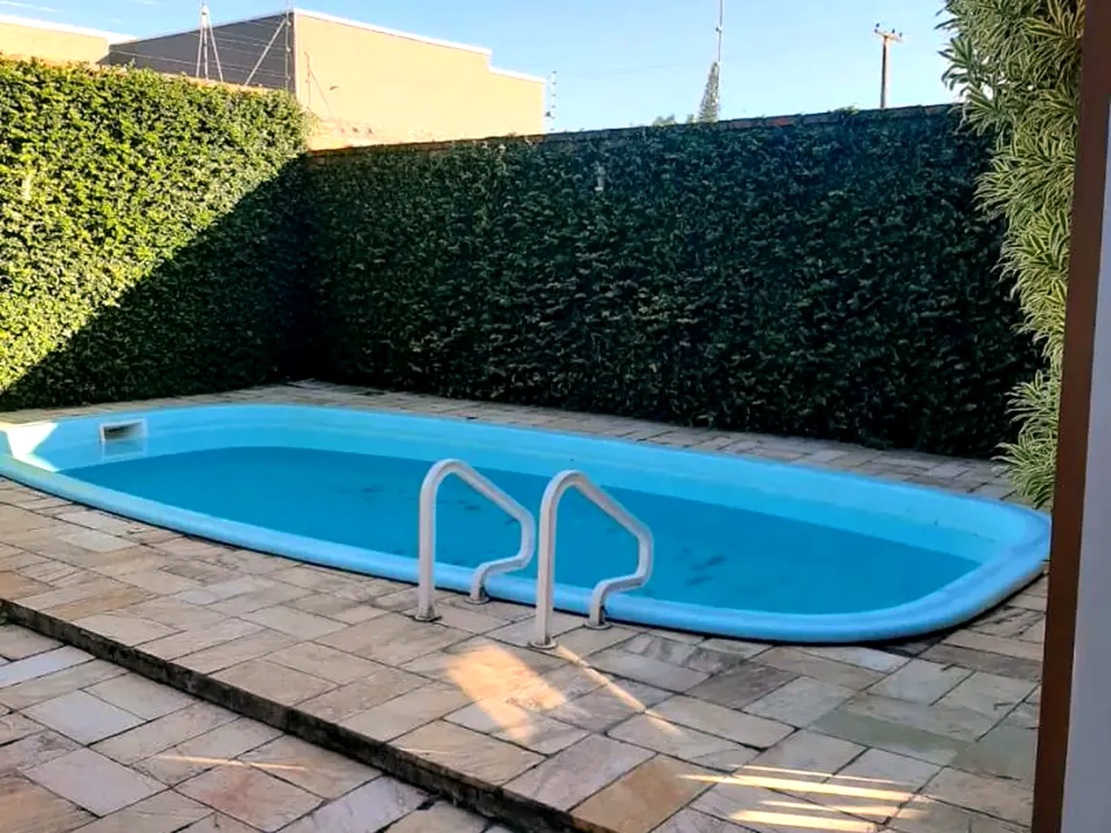 Piscina no pátio lateral, cercada por cerca-viva alta.