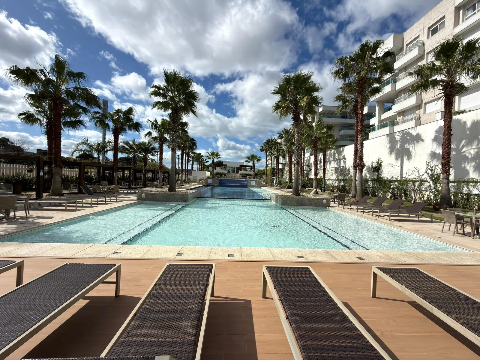 Piscina externa do Atlântida Green Square, ladeada por palmeiras e deck de madeira com espreguiçadeiras.