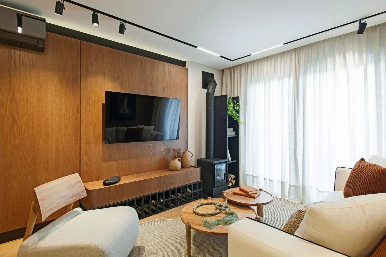 Sala de estar com painel de madeira, TV e cortina até o chão.