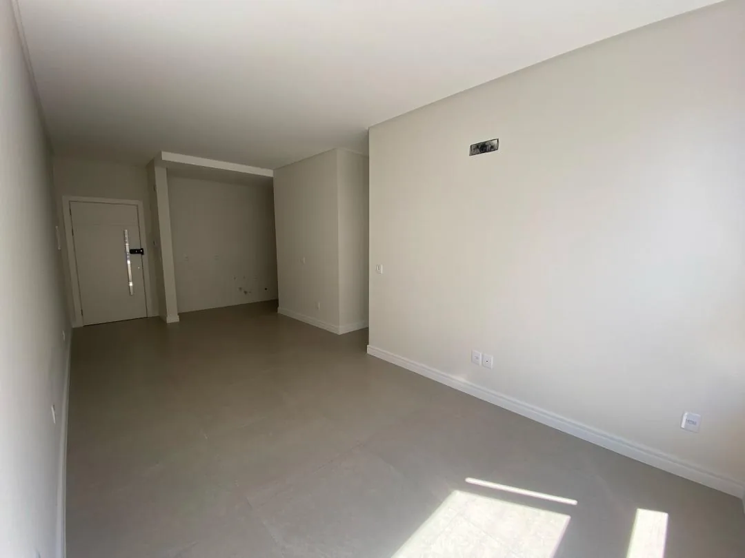 Sala vazia com paredes claras e piso porcelanato cinza.