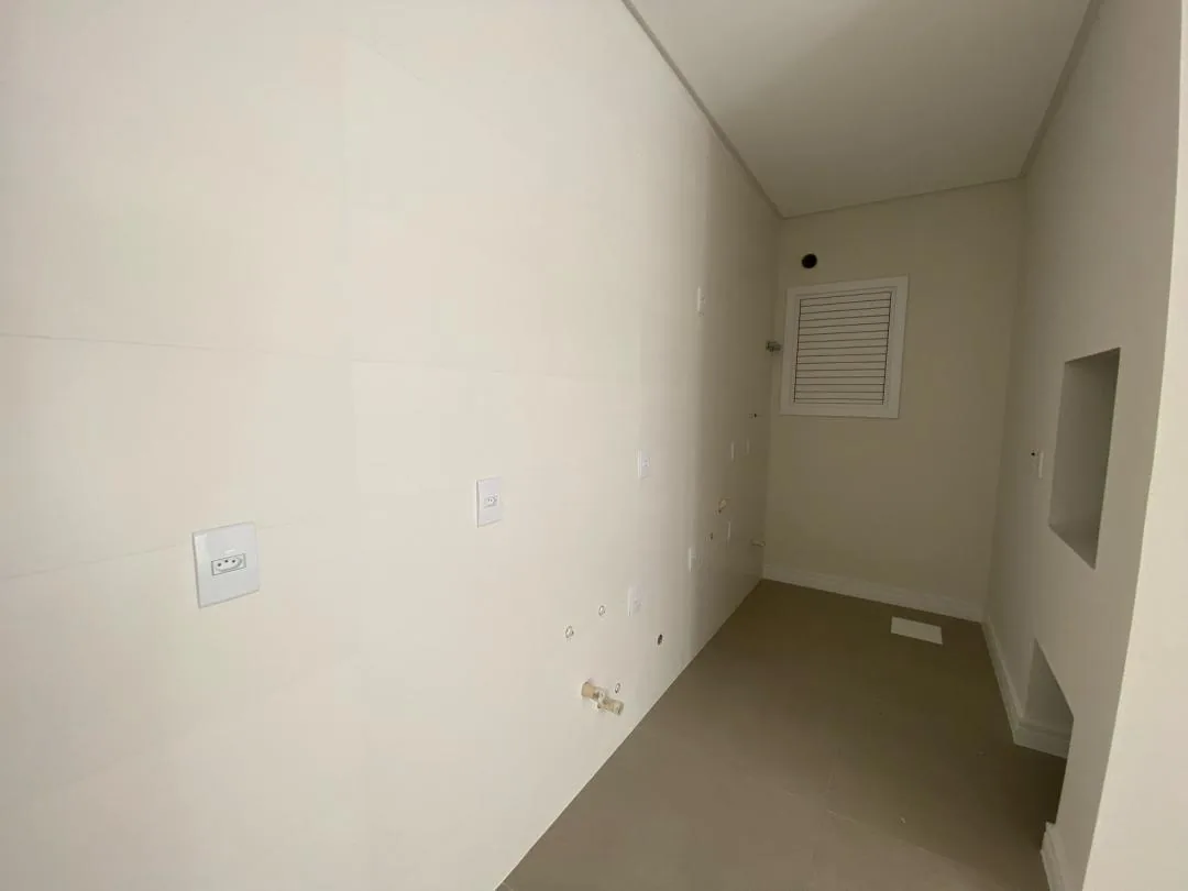 Área de serviço vazia com parede em porcelanato e janela basculante.
