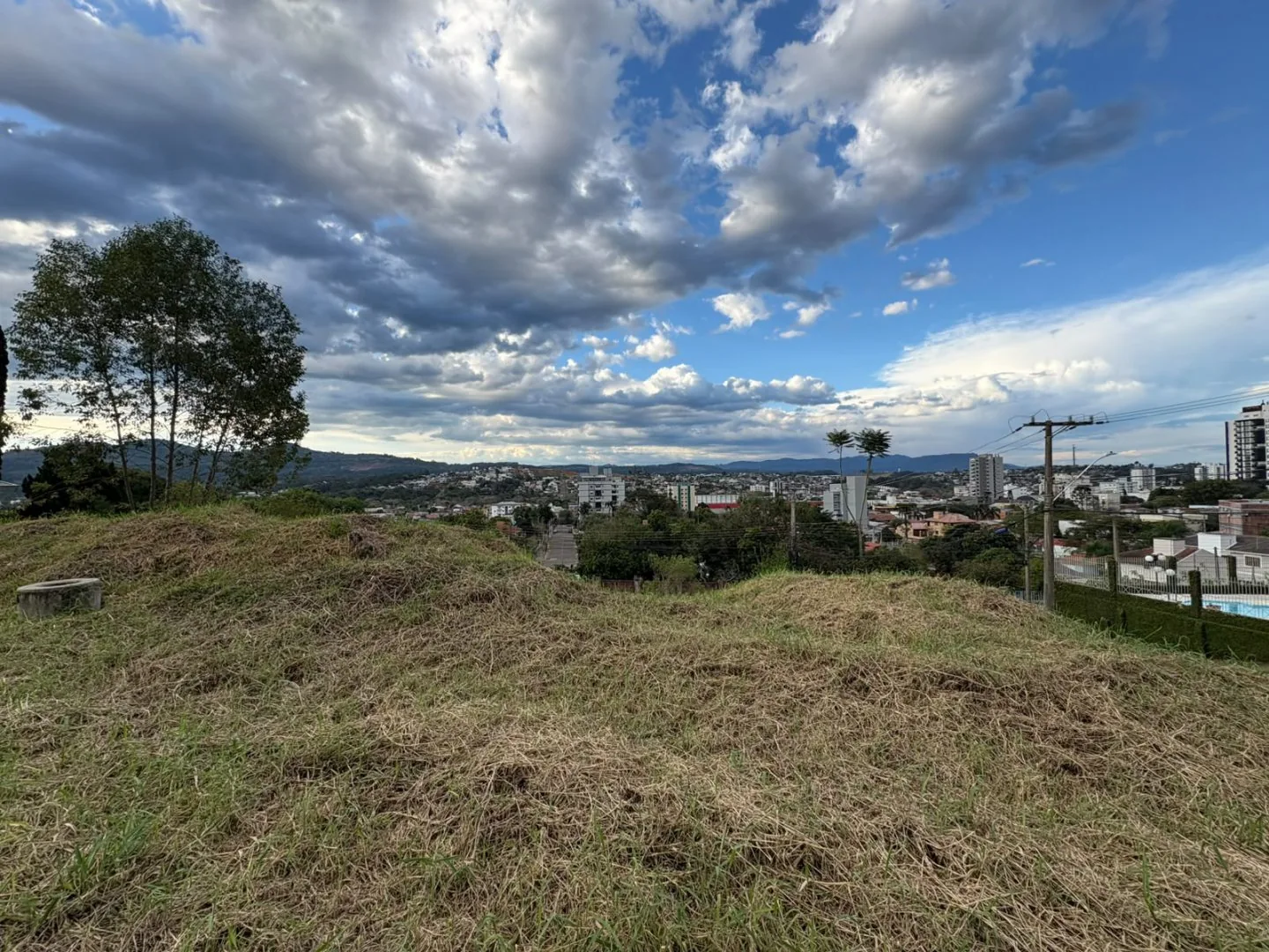 Terreno gramado no alto, com a cidade e as montanhas ao fundo.
