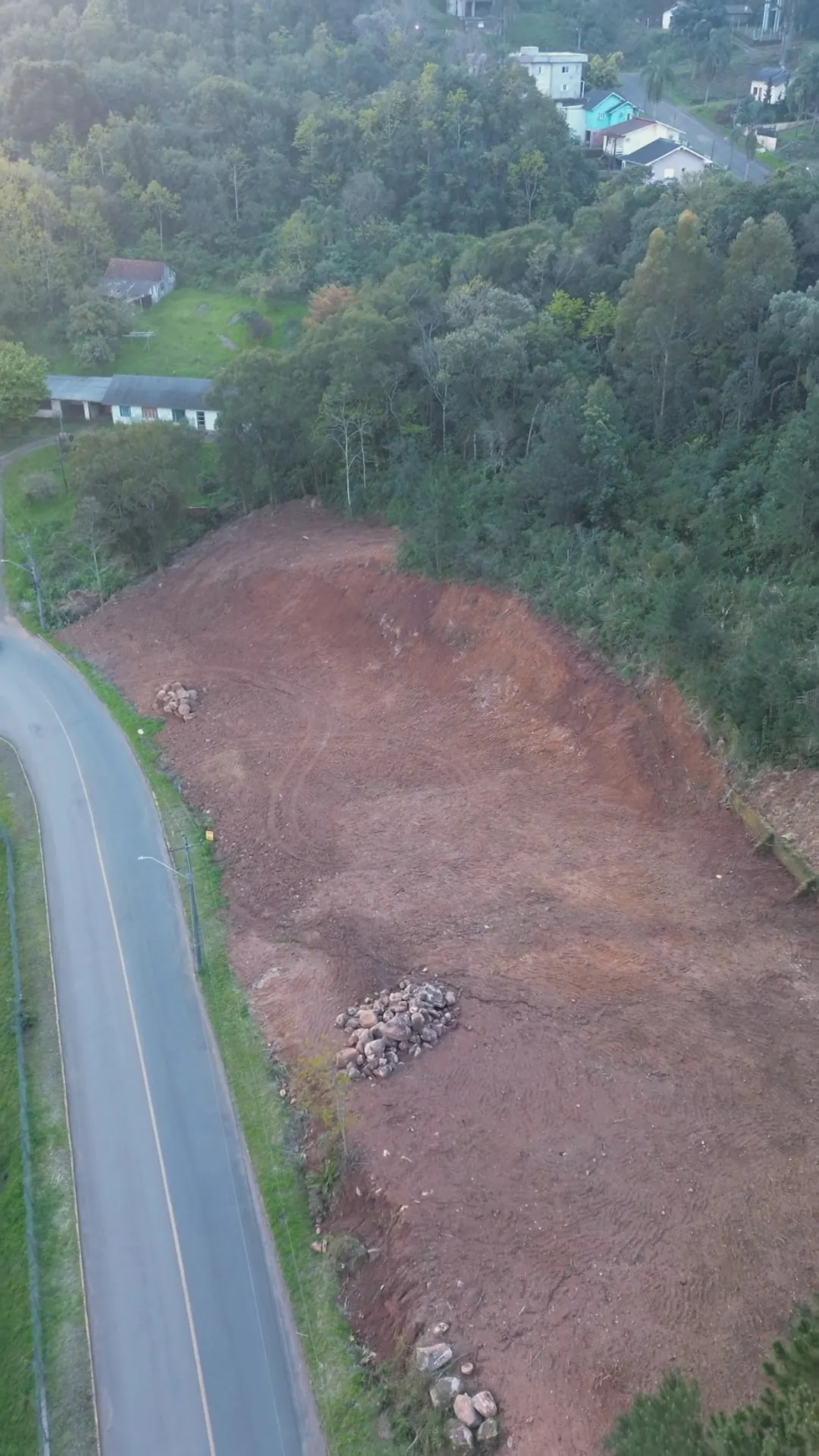 O terreno visto do alto, com a rua asfaltada à esquerda e a mata em volta.