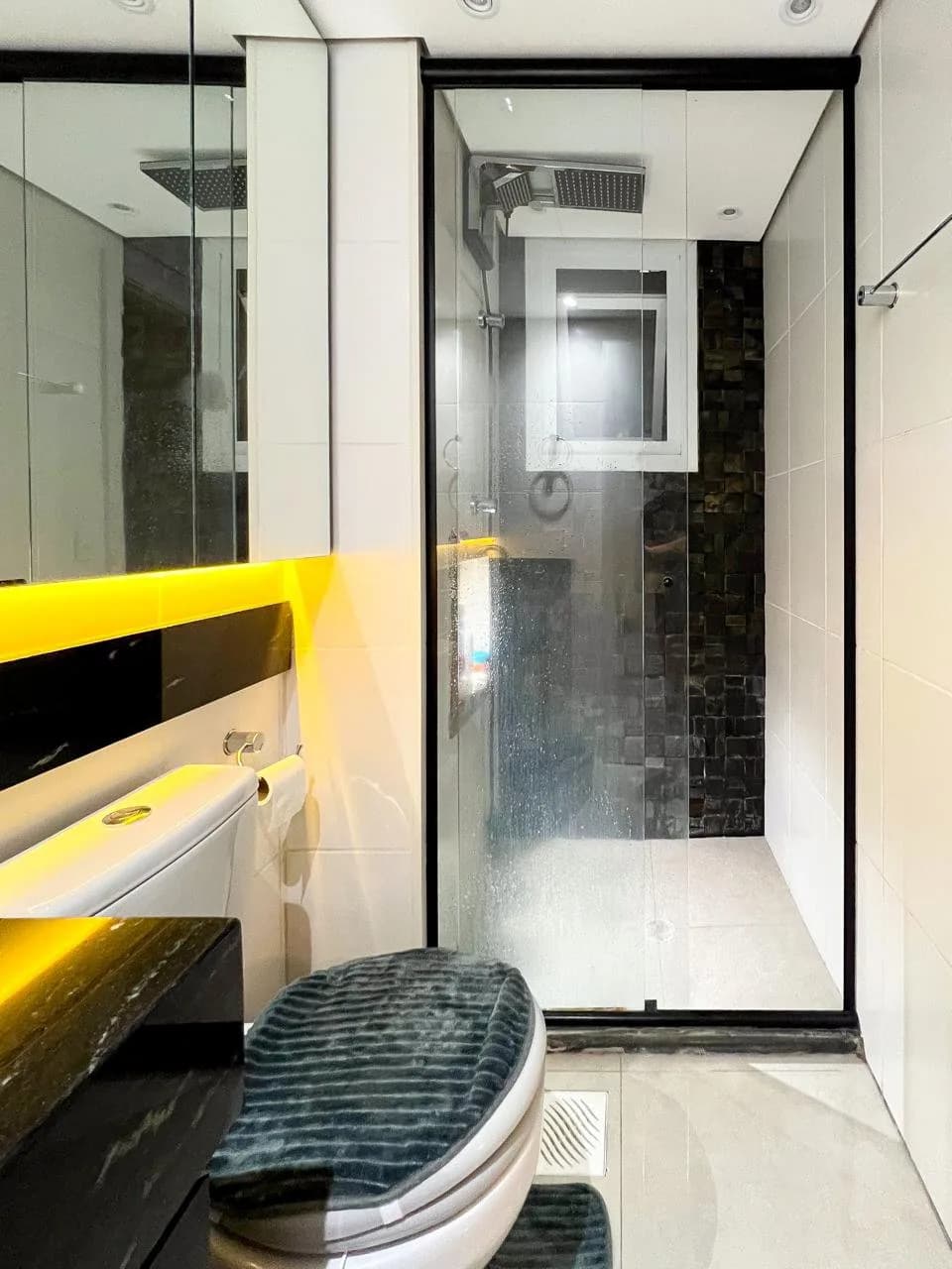 Banheiro social, com box de vidro, ducha e detalhe em amarelo na parede.