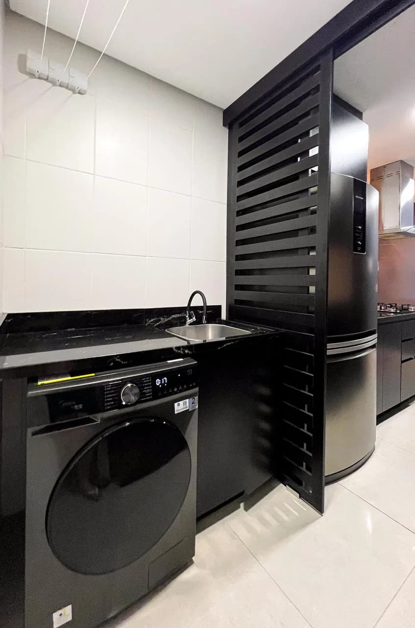 Área de serviço equipada, com lavadora e secadora embutidas em armário preto.