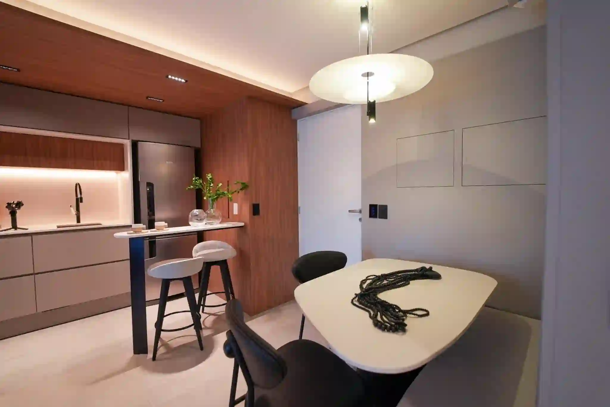 Sala de jantar integrada à cozinha do apartamento decorado, com pendente sobre a mesa.