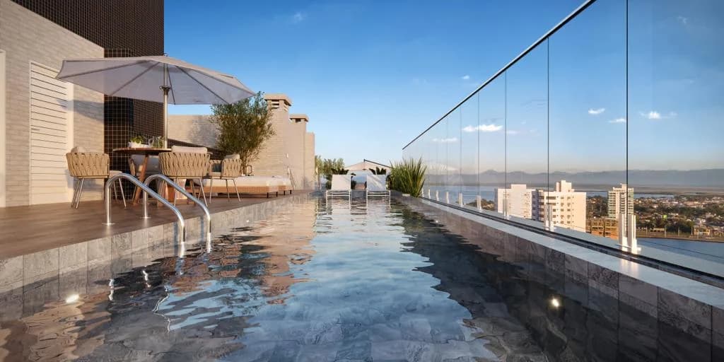 Perspectiva da piscina de borda infinita no rooftop, com a cidade e o mar ao fundo.